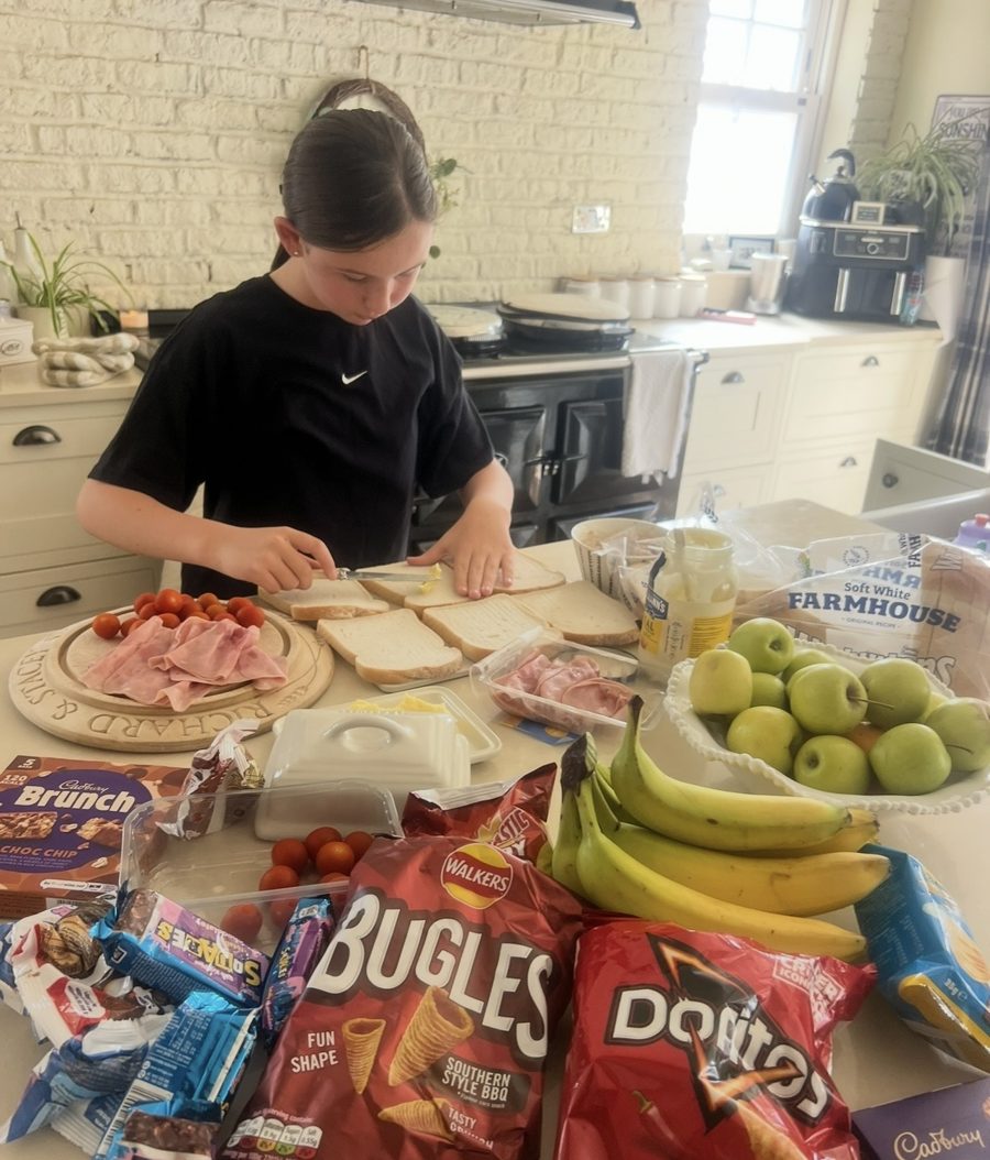 Elsie making a big batch of sandwiches with fruit, crisps and snack bars laid out to hand out