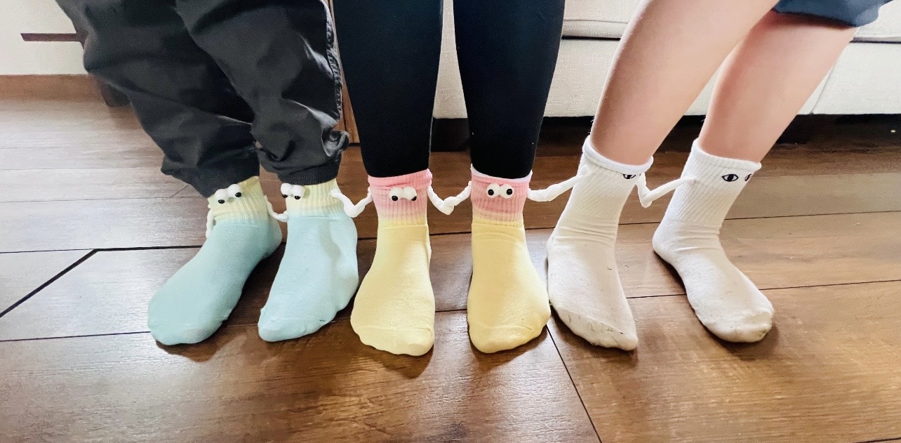 Three people standing in a row wearing cheerful socks with googly eyes and little arms that hold hands with the next pair